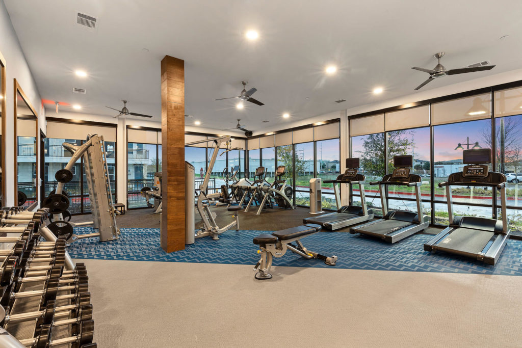 Fitness area with free weight, cardio machines, ceiling fans and floor to ceiling windows
