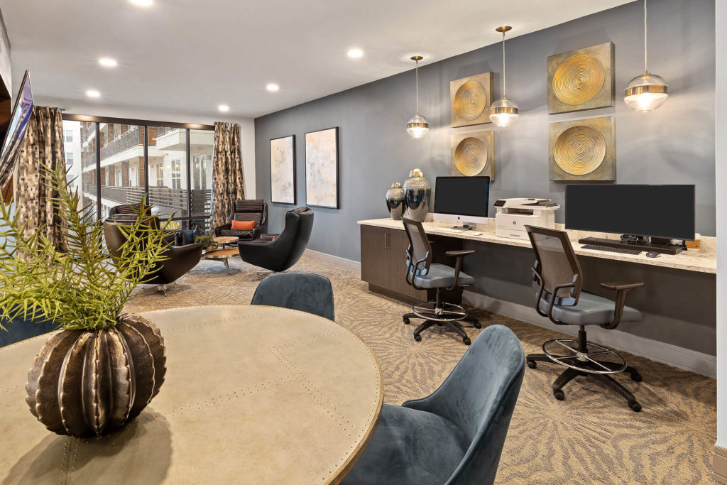 Clubhouse computer area with Mac and PC computers, desk chairs, pendant lighting, and additional roundtable seating