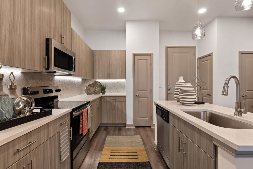Kitchen with wood-like floors, island with large single basin sink, pantry and stainless-steel appliances