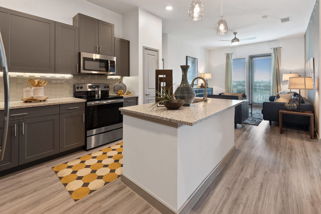 Open concept kitchen and living area with stainless-steel appliances, kitchen island, pendant lighting, wood-like floors, and door to patio/balcony