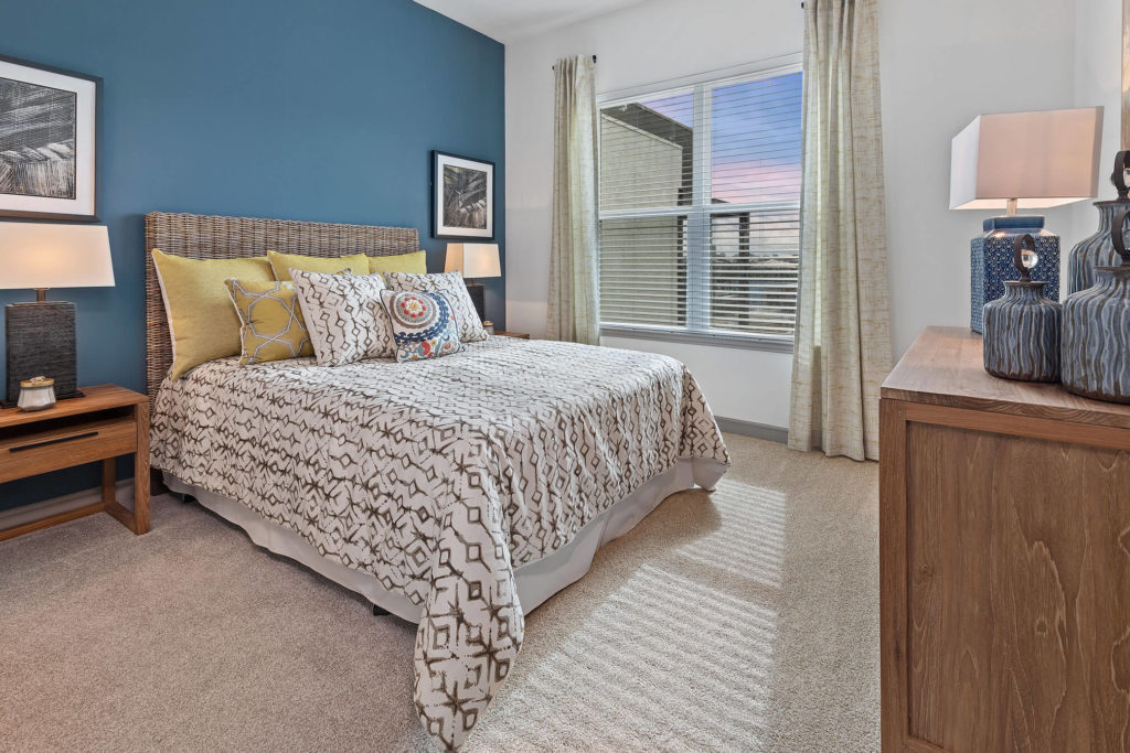 Bedroom with plush carpeting, queen sized bed, nightstands, large window, and blue accent wall