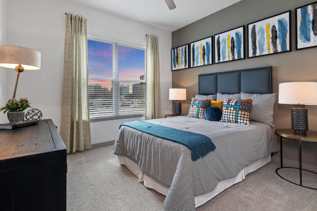 Bedroom with gray accent wall, large window with view, plush carpeting, modern furniture and ceiling fan
