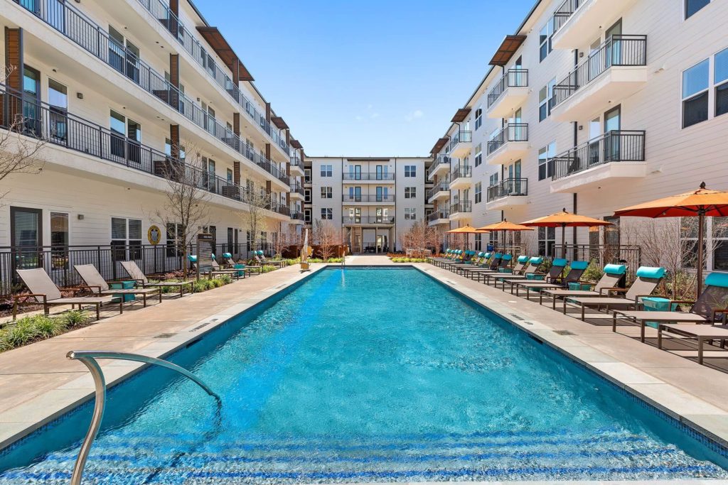 Community buildings surrounding resort-like pool with stairs, umbrellas, and lounge furniture