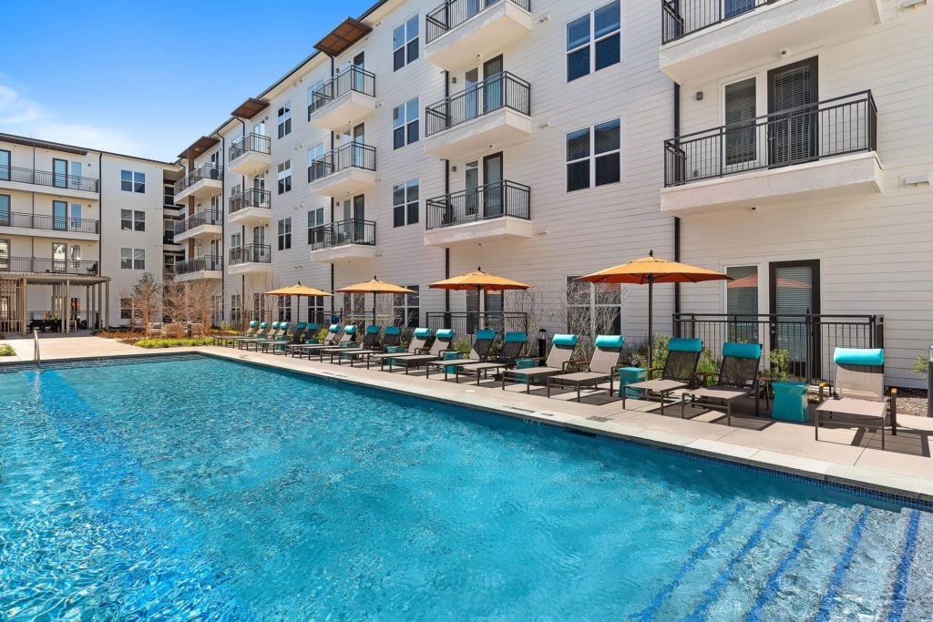 Daytime shot of resort-style pool with stairs and lounge seating with umbrellas