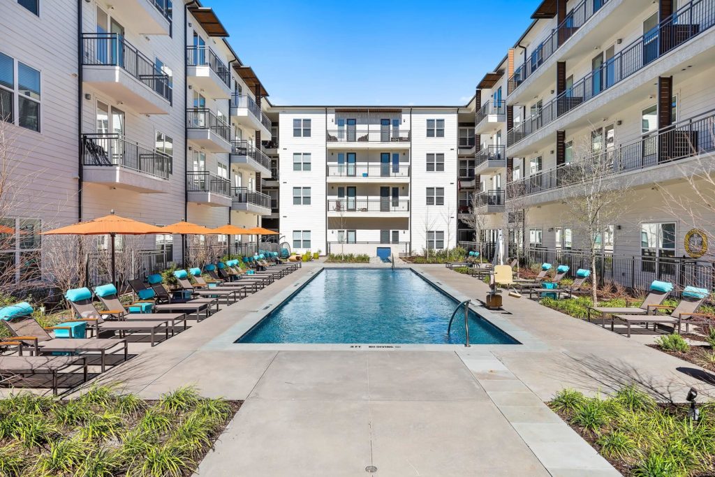 Daytime shot of resort-style pool with lounge seating, landscaping, umbrellas, and gate