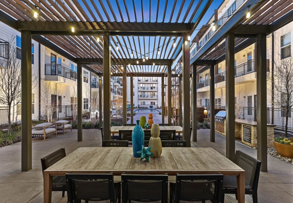 Outdoor courtyard area with covered seating and tables, patio lights, and community grill