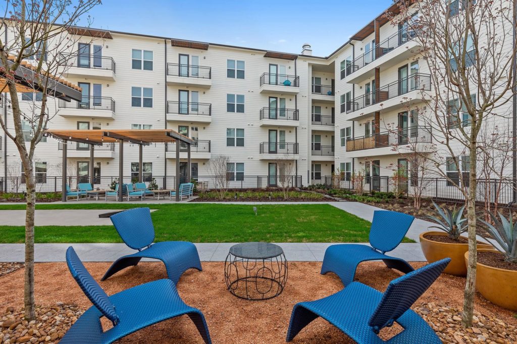 Outdoor courtyard with patio seating, lush landscaping, small yard with cornhole and covered seating