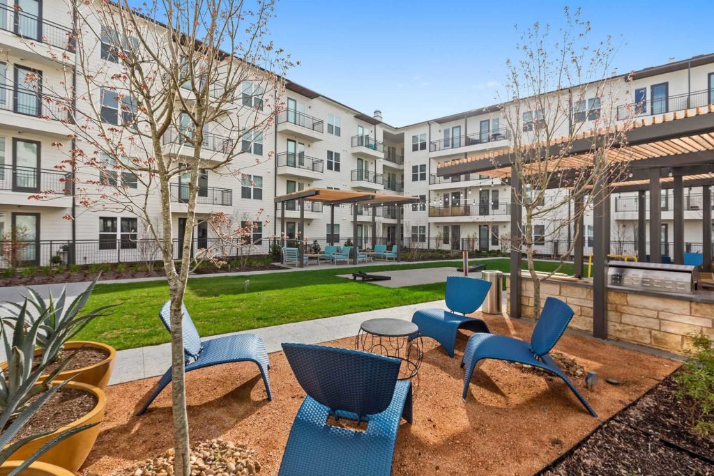Outdoor courtyard with patio seating, community grill, small yard with cornhole and covered seating